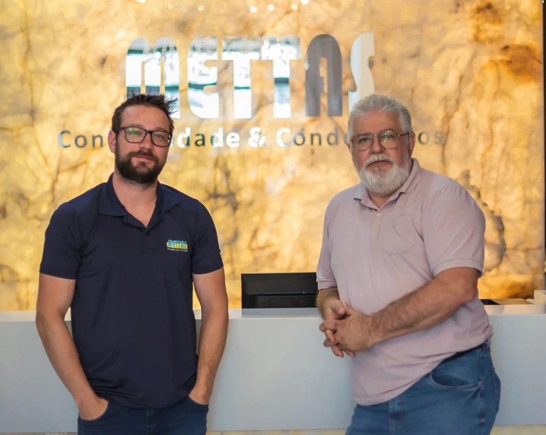 Sócios da Mettas na recepção do escritório, em frente ao logo da empresa em Itapema